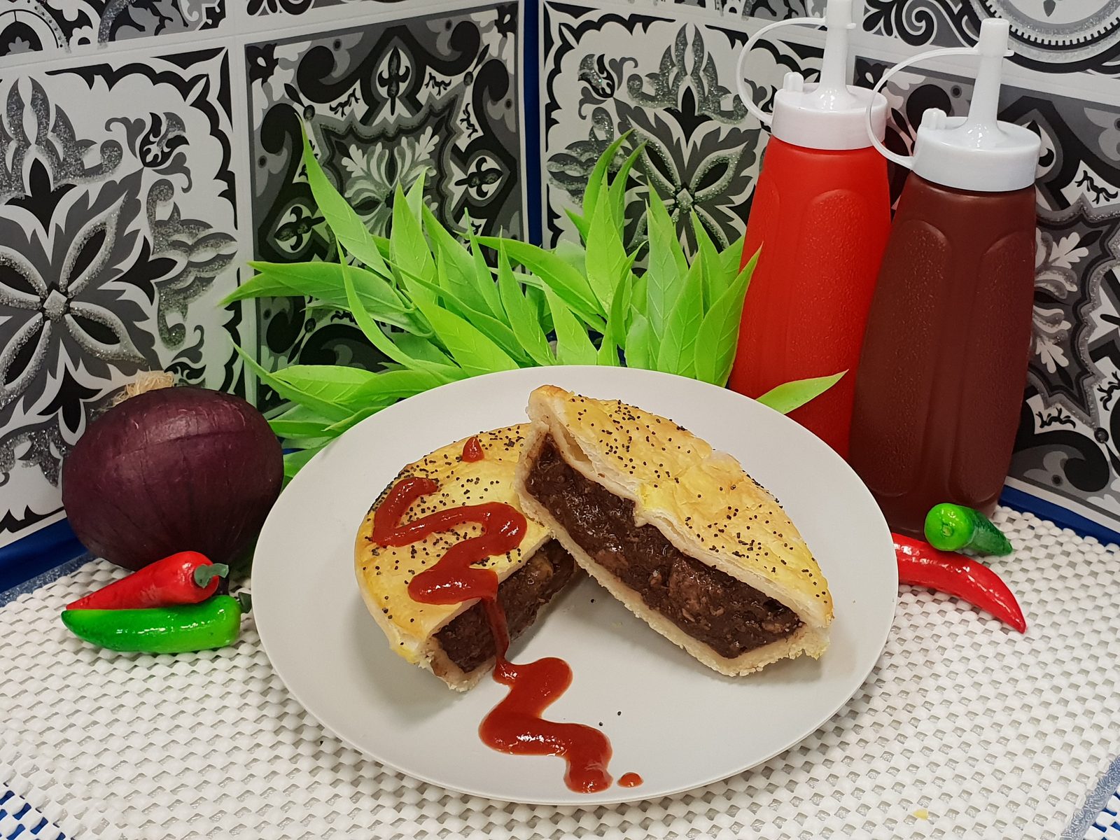 Simply Pies flavoured meat pie cut open with tomato sauce, served on a plate with sauce bottles